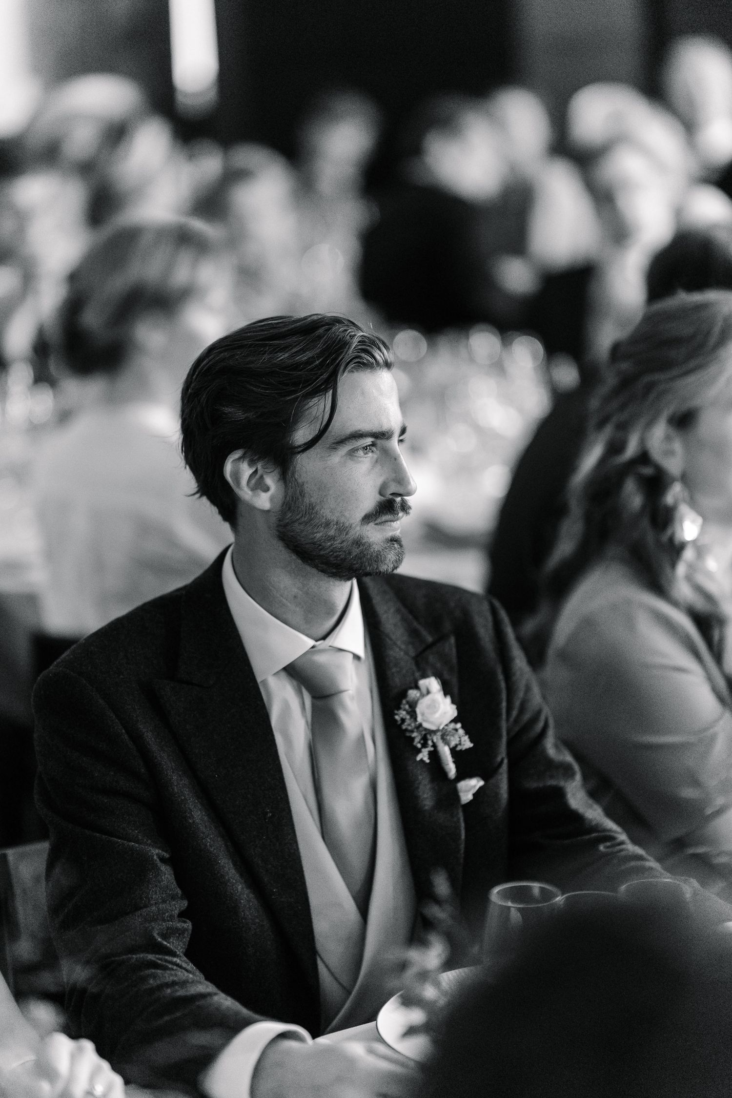 Black and white sequence of a man in a dark suit and tie sitting and looking to the side at an event.
