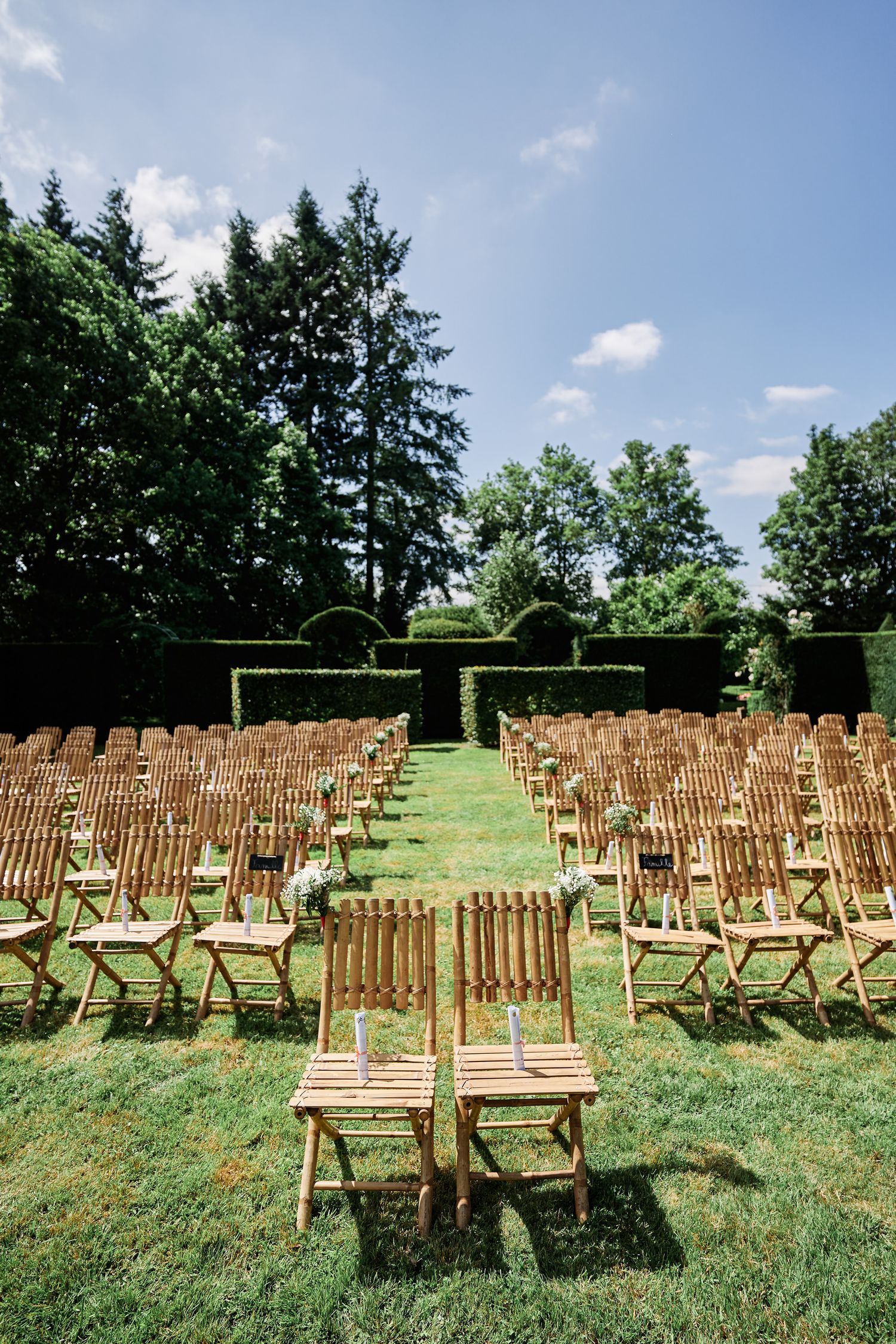 Rows of wooden folding chairs arranged on a grassy hillside for an outdoor wedding ceremony under blue summer skies.
