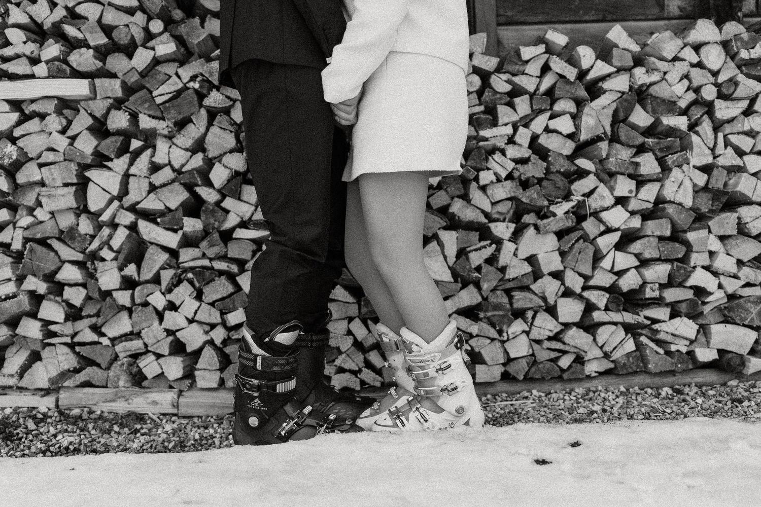 A person in white stands against a rustic stacked firewood wall backdrop creating a striking contrast.