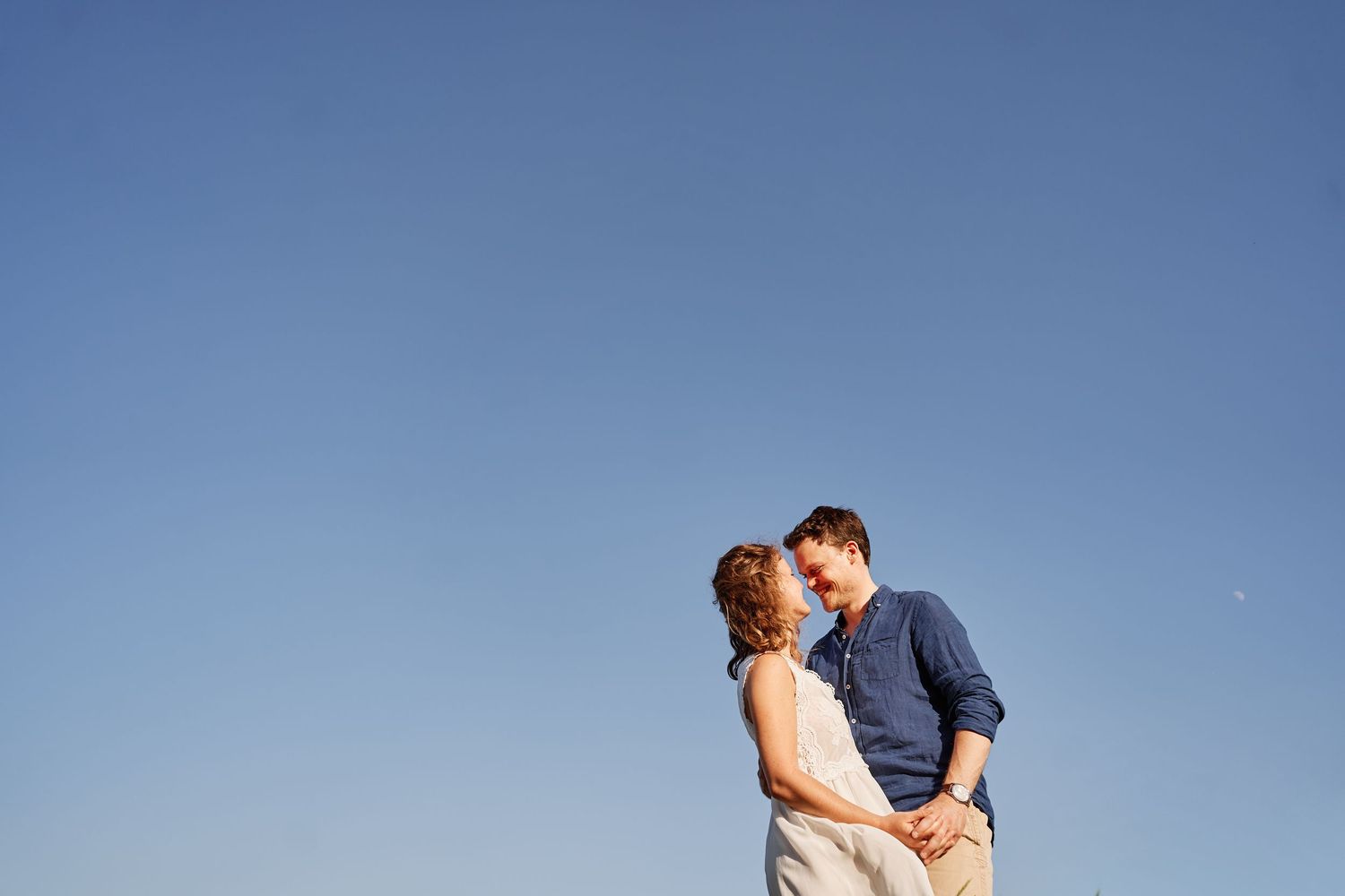 A couple embraces against a bright blue sky on a sunny day.