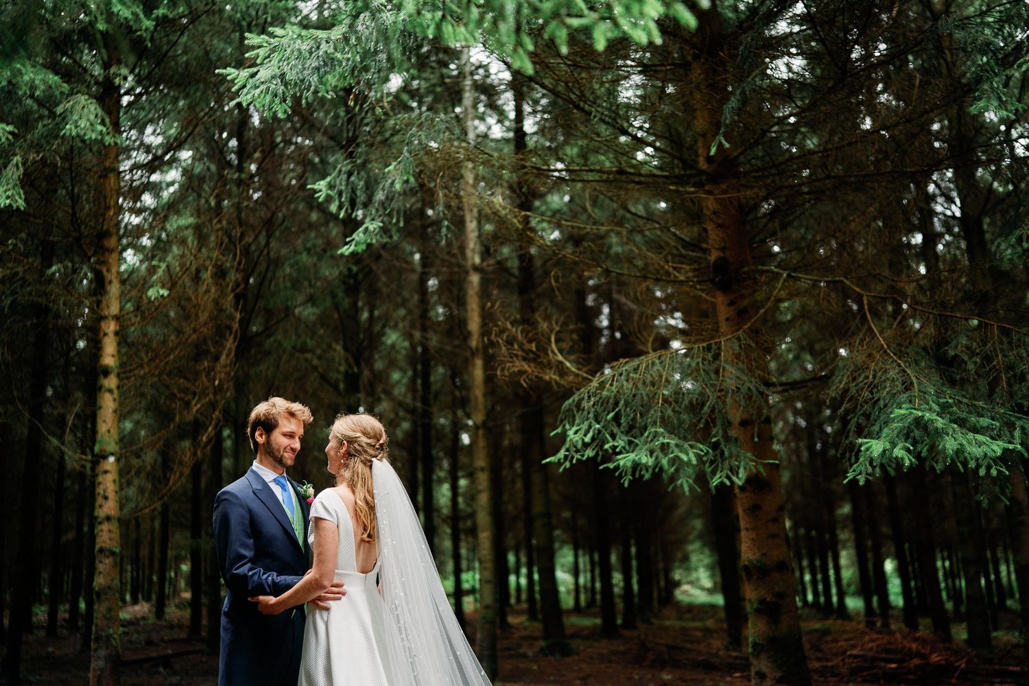 A romantic couple in wedding attire shares intimate moments while walking through a serene forest setting.