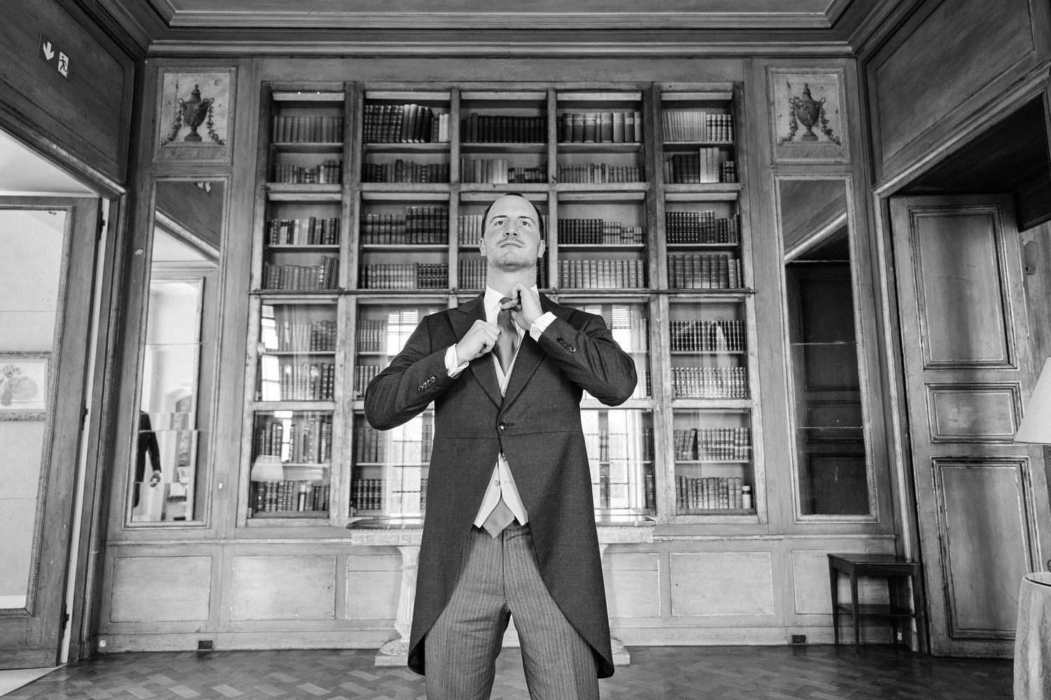 A black and white photo collage shows a person in formal attire in different poses against a library backdrop.