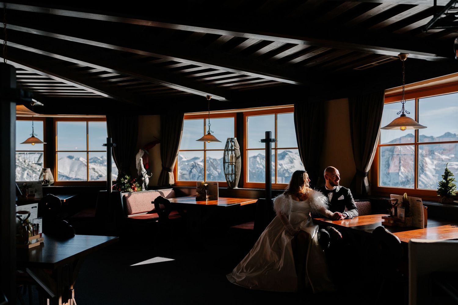 Cozy modern restaurant interior with wooden tables, pendant lights, and large windows overlooking a scenic view.