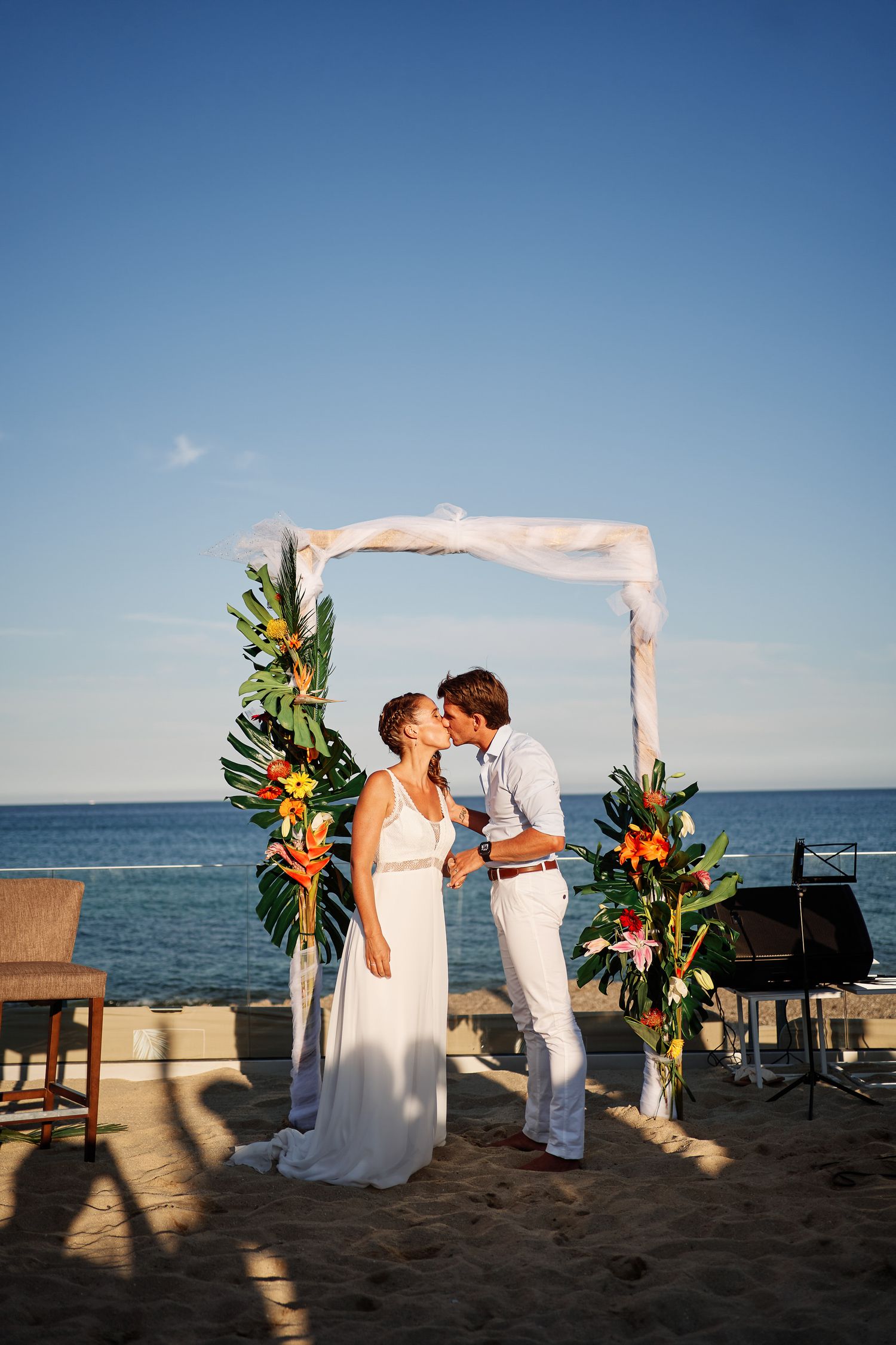 A beachside wedding ceremony unfolds in a series of sunset photos showing a couple under a floral arch by the ocean.