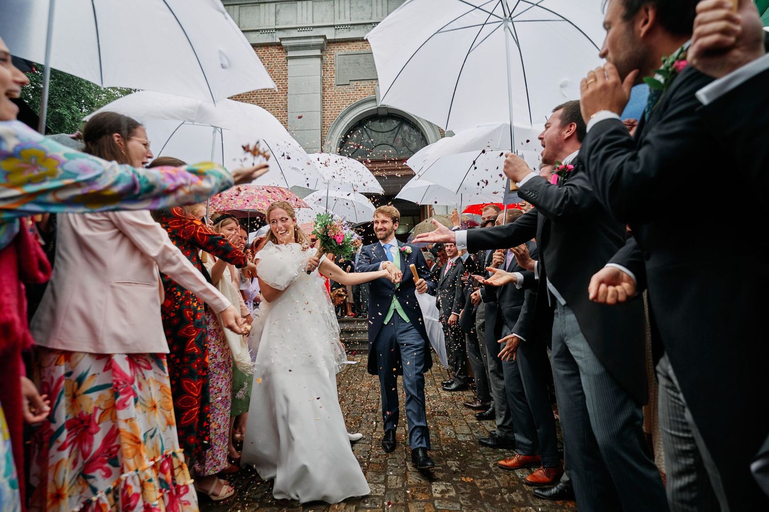 Wedding guests with white umbrellas gather outside in the rain during an outdoor celebration.
