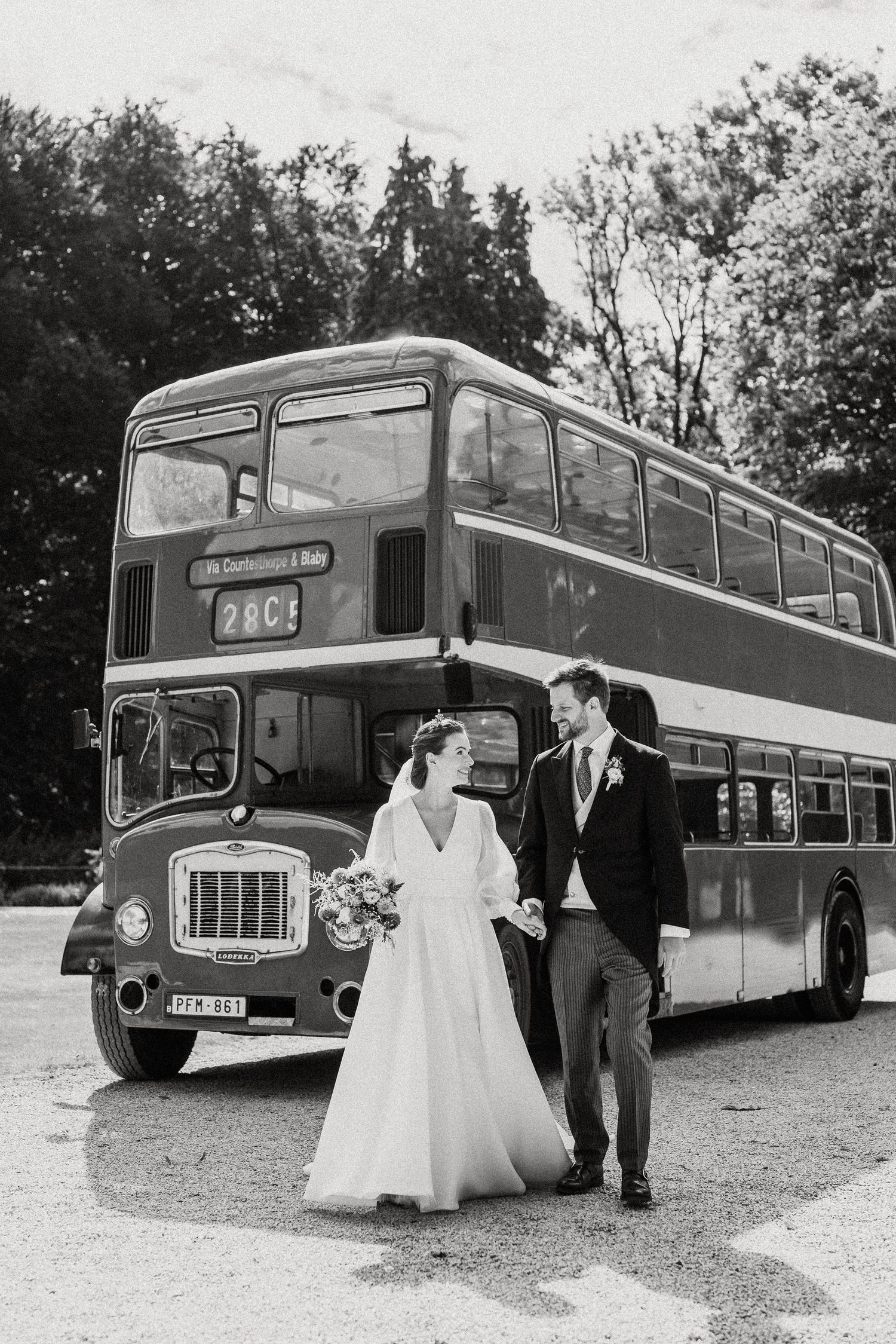 A vintage red double decker bus serves as backdrop for a romantic black and white wedding photo.