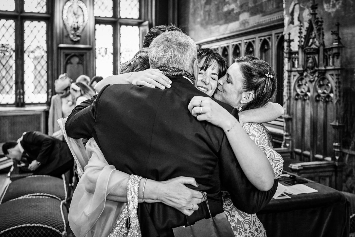 Black and white candid photo of an emotional moment between three people embracing in what appears to be a church setting.