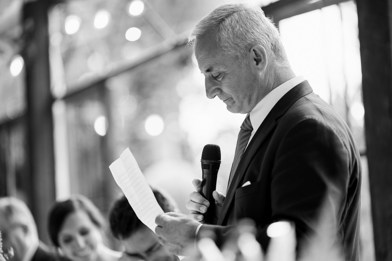 A black and white photo shows guests socializing at an elegant event with bokeh lights in the background.