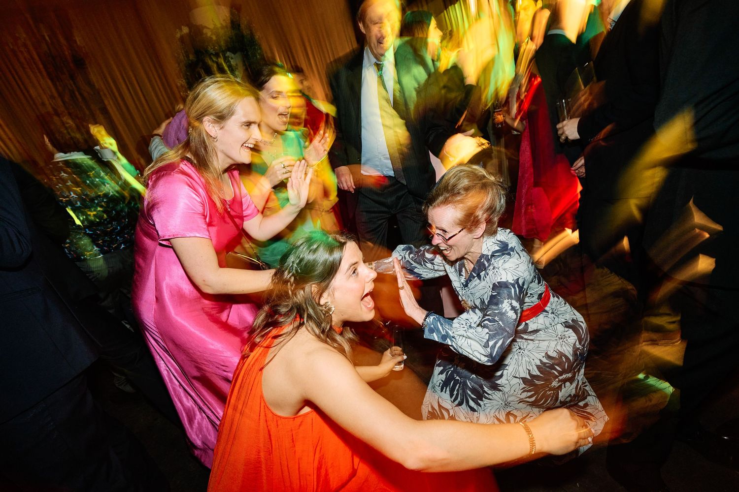 People dancing and celebrating energetically at a party with colorful lighting and dynamic movement.