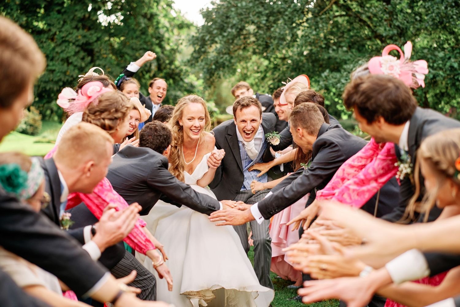 A group of wedding guests lean in to catch the bouquet toss during an outdoor garden celebration.