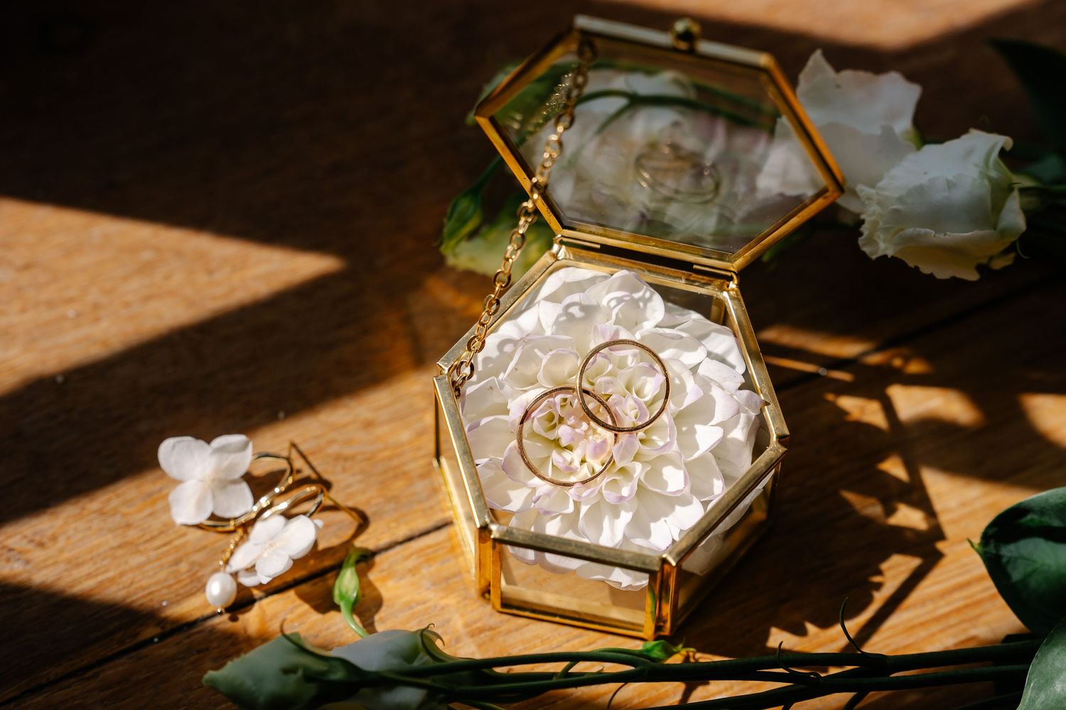 Glass jewelry box with geometric edges sits on wooden surface in warm sunlight casting dramatic shadows.