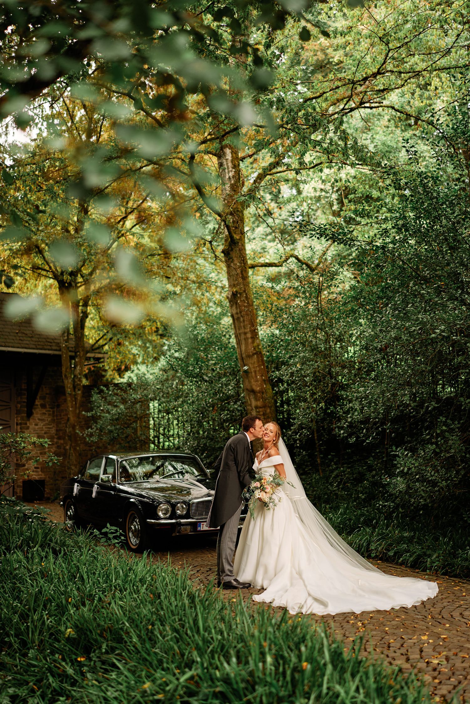 A classic vintage car sits elegantly among lush greenery during a wedding photoshoot in a garden setting.