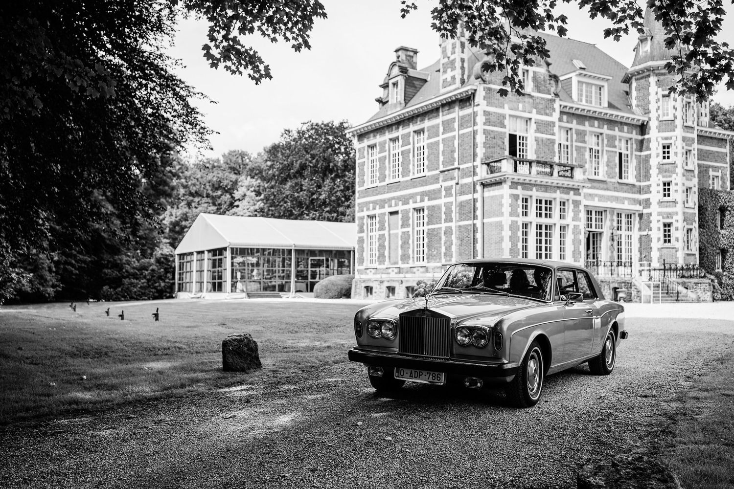 A vintage car parked outside a grand historic building with trees in the background.