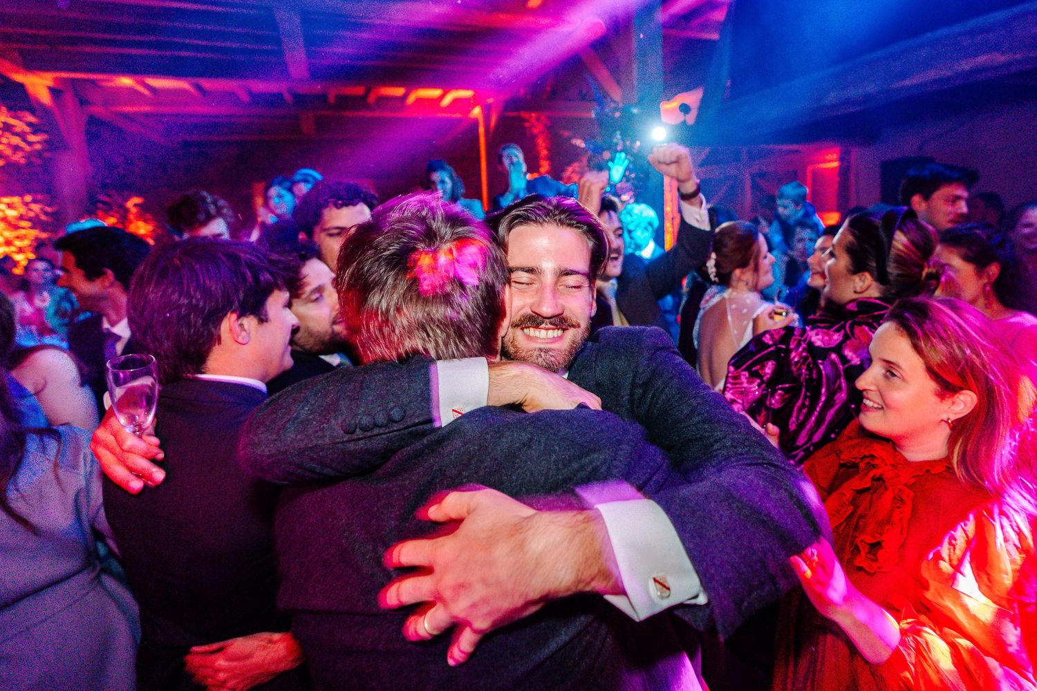 Crowded nightclub dance floor illuminated by vibrant pink and blue lights as people dance and socialize.