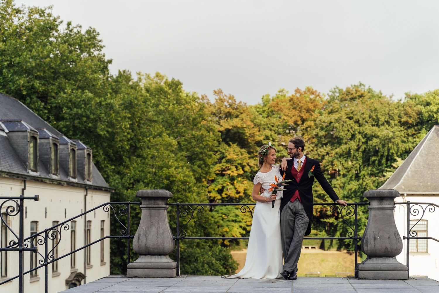 Wedding couple poses at an elegant venue with stone urns and white pillars during an outdoor celebration.