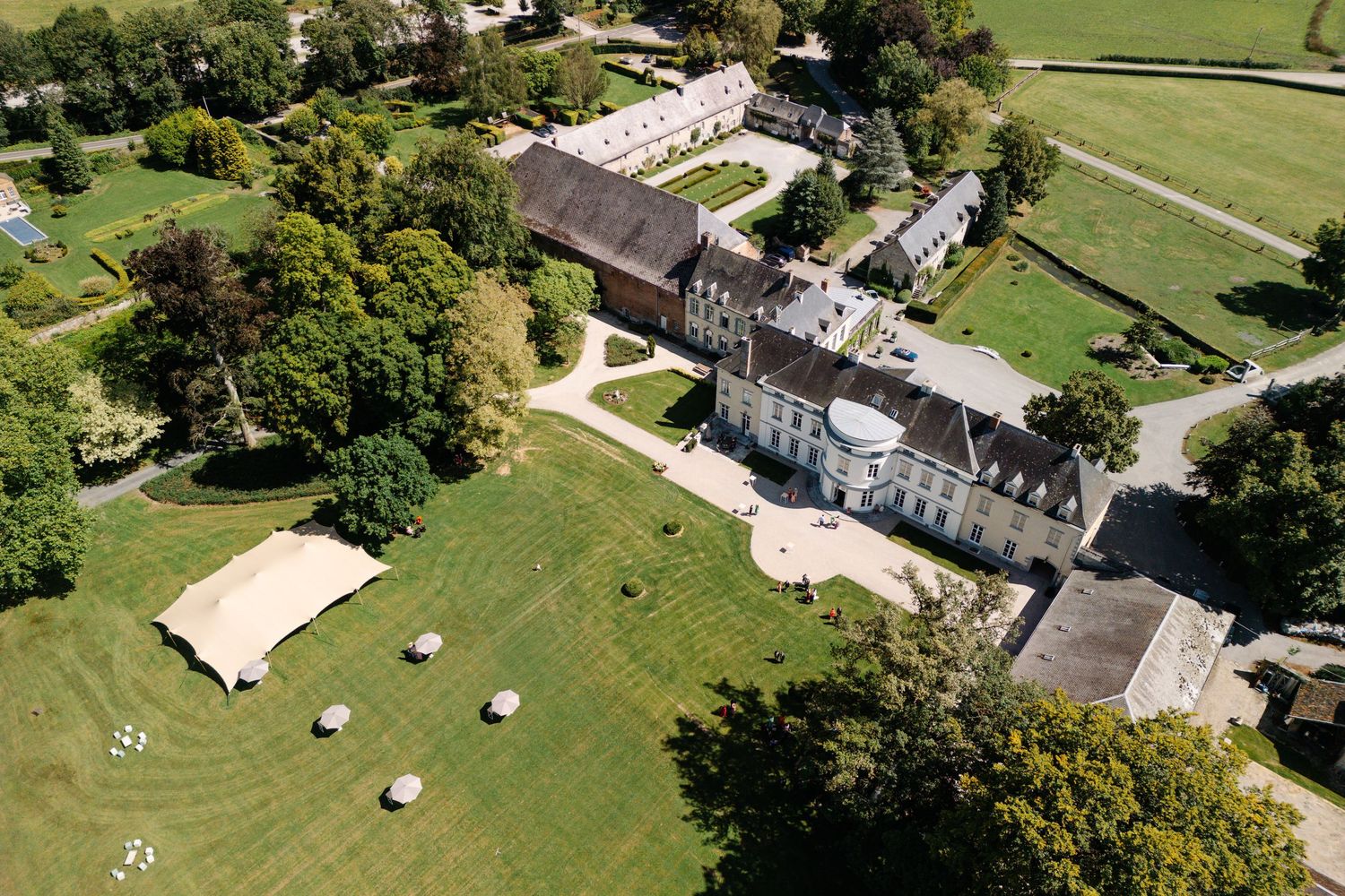 Aerial view of a historic manor house with manicured grounds and white event tents set up on the lawn.