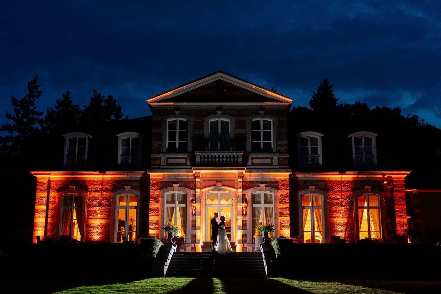 Wedding venue illuminated at night with warm orange lighting and silhouettes against the building's facade.