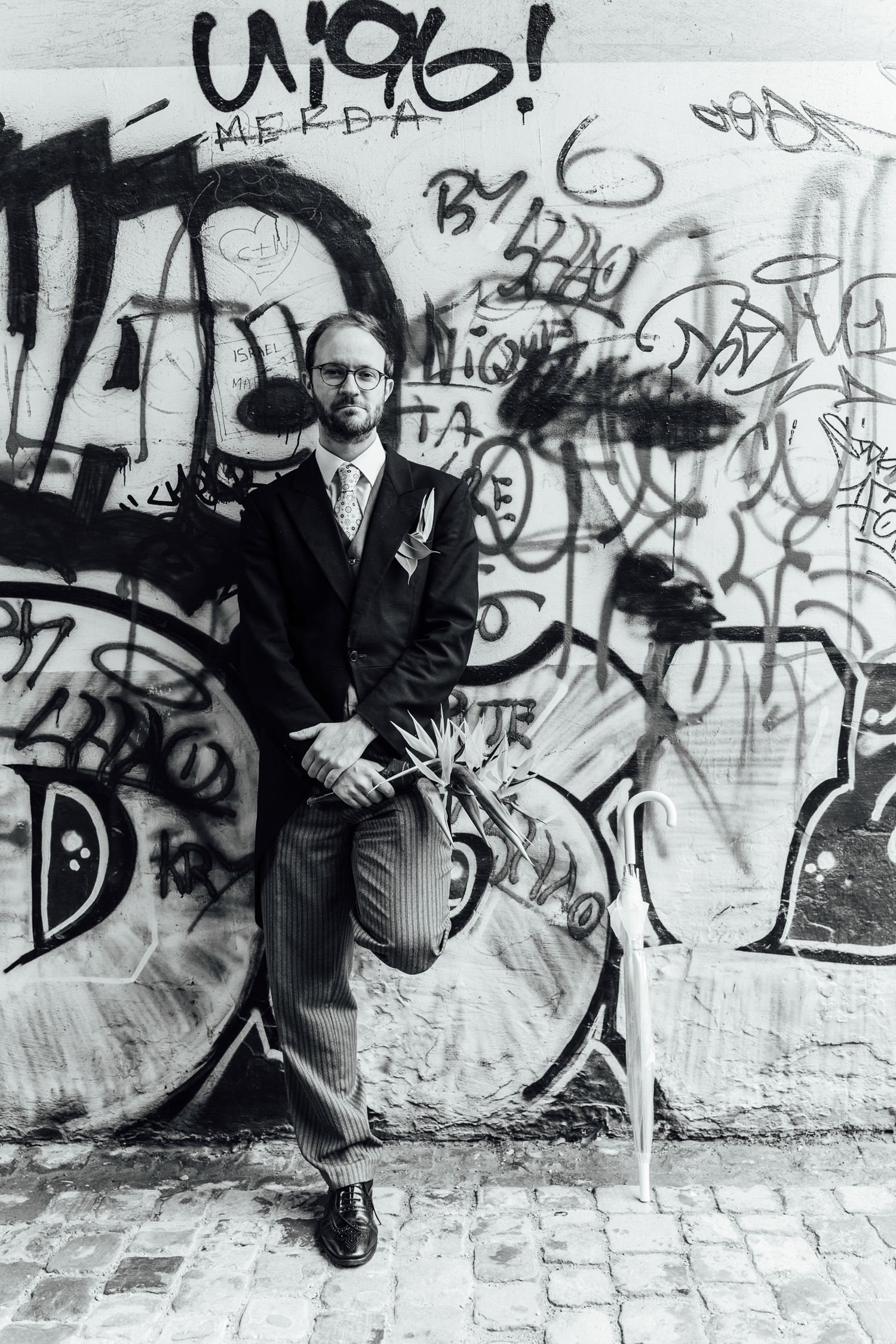 Black and white photo sequence showing a person in a suit sliding down along a graffiti-covered wall.