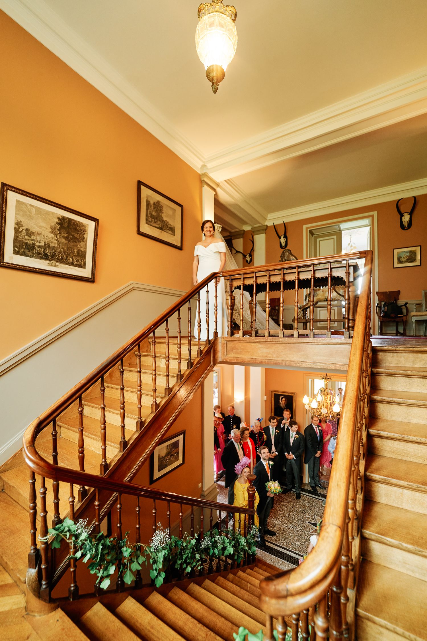Elegant curved wooden staircase in historic home with warm yellow walls and decorative greenery along banister.