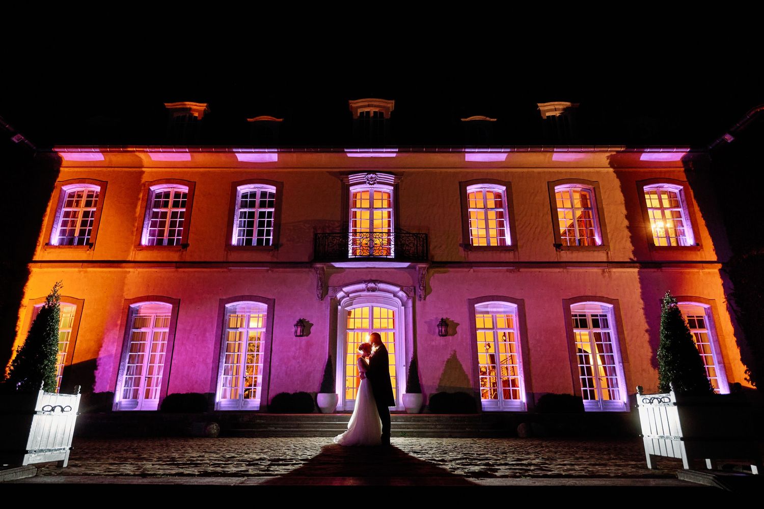 Historic mansion illuminated with vibrant orange and purple lights creating a dramatic nighttime display.