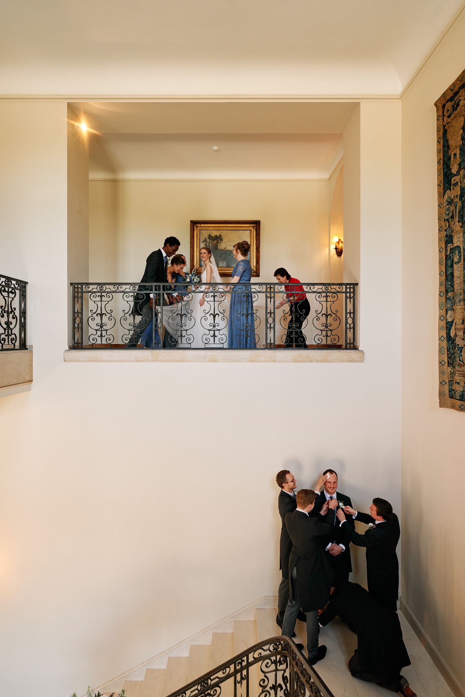 People gather and interact along an elegant white hallway with ornate iron railings and decorative artwork on the walls.