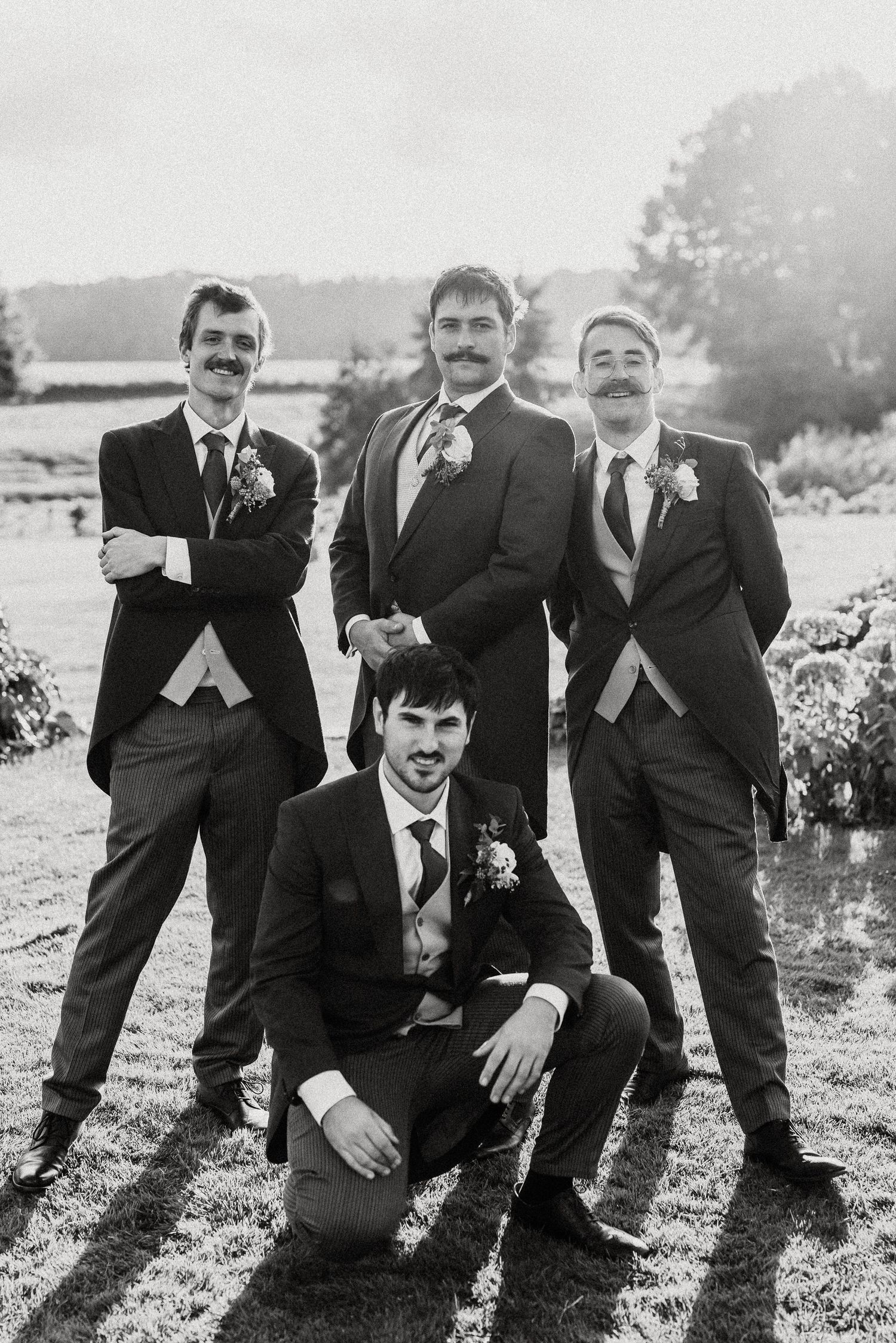 A group in formal suits strikes playful poses together in a black and white outdoor photo sequence.