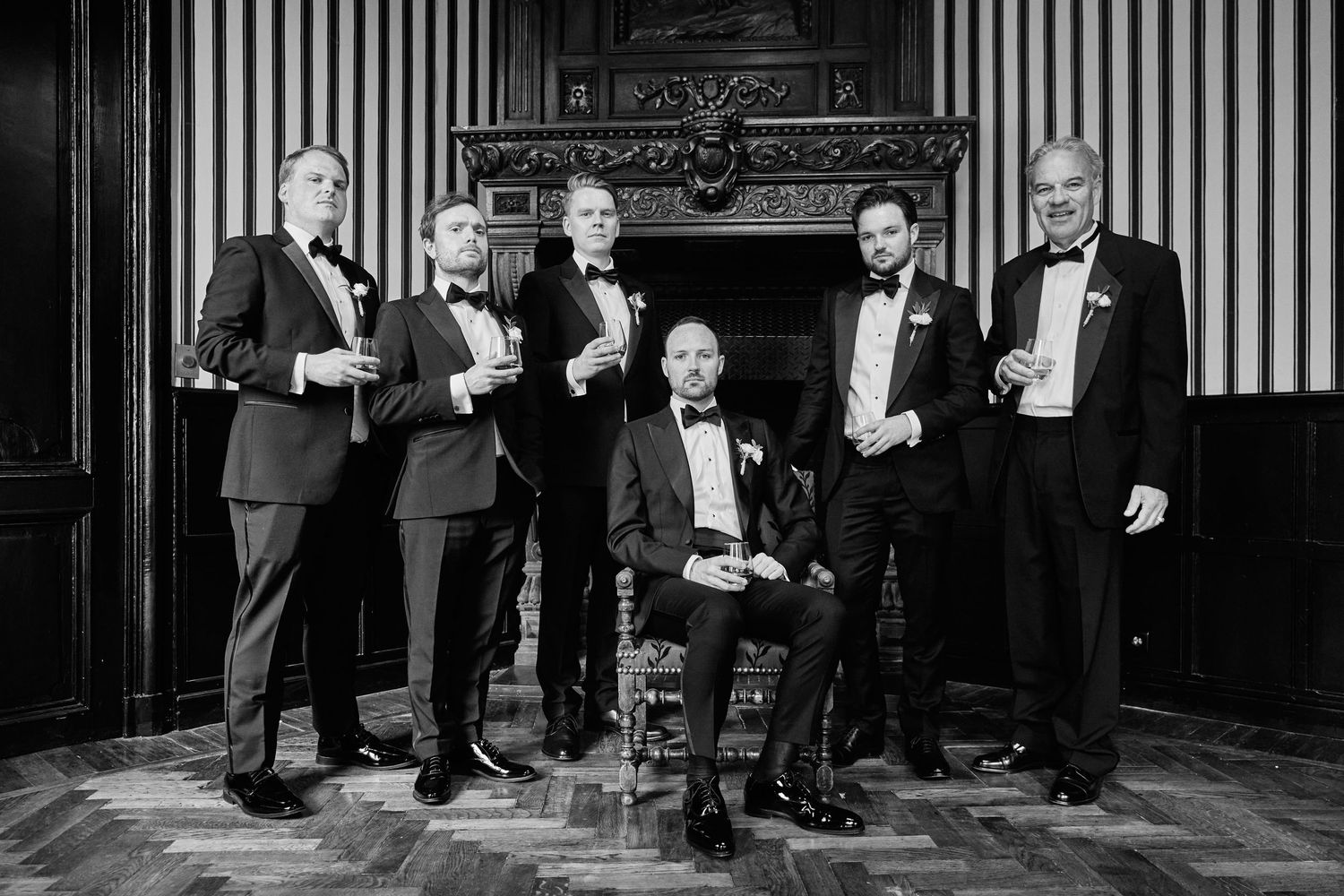 Vintage black and white photograph showing formal gathering of people in tuxedos in an ornate room.