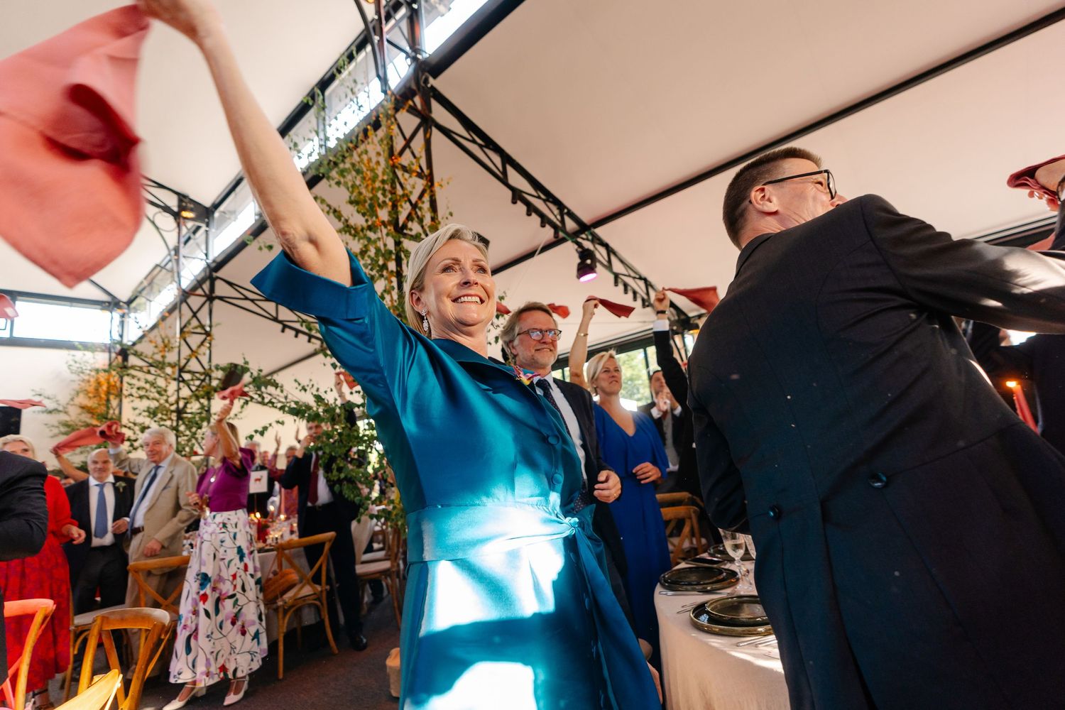 People dancing and celebrating with raised arms at an outdoor event under a covered venue area.