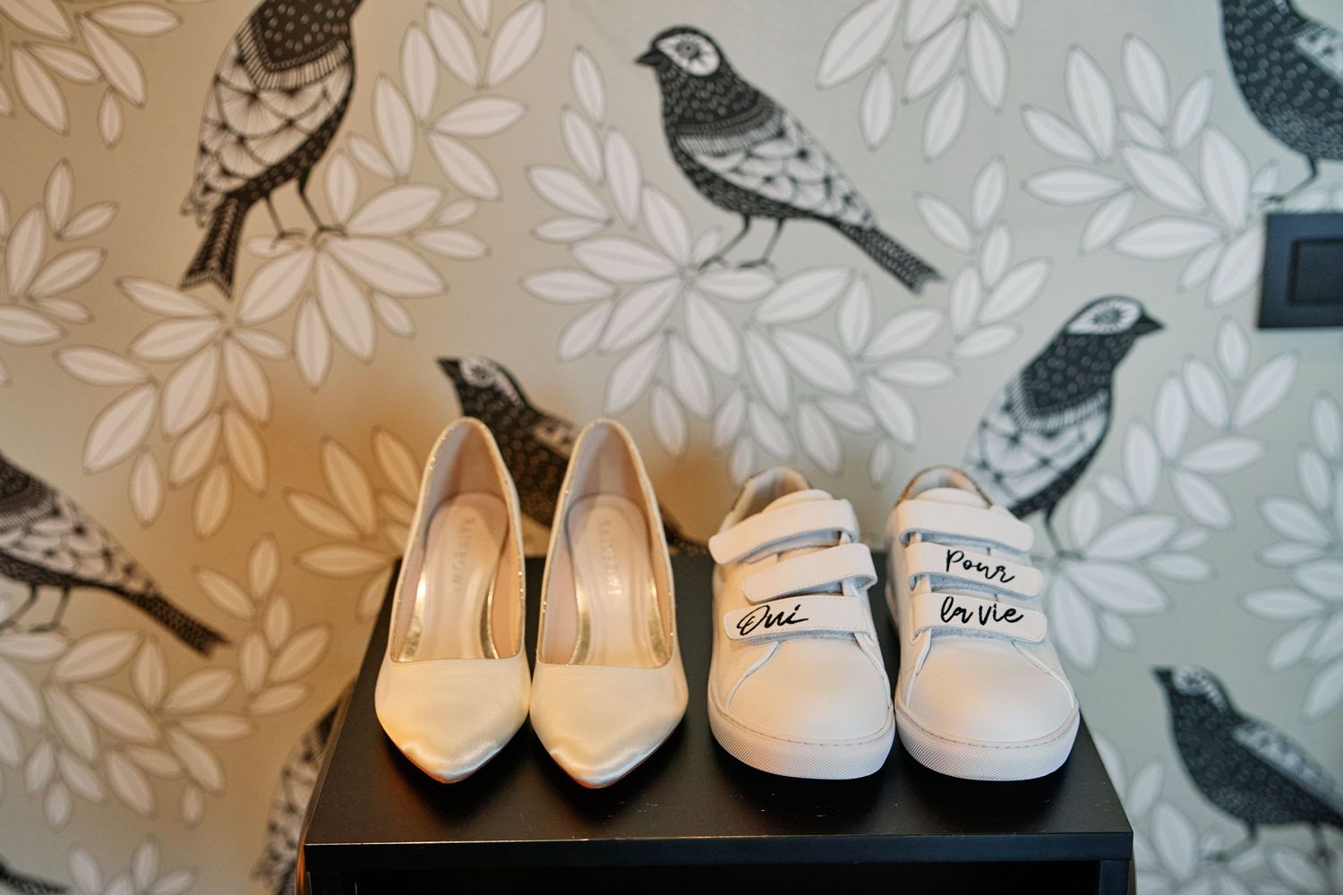 Five pairs of elegant beige and cream colored women's high heel shoes arranged in a row against a floral wallpaper background.