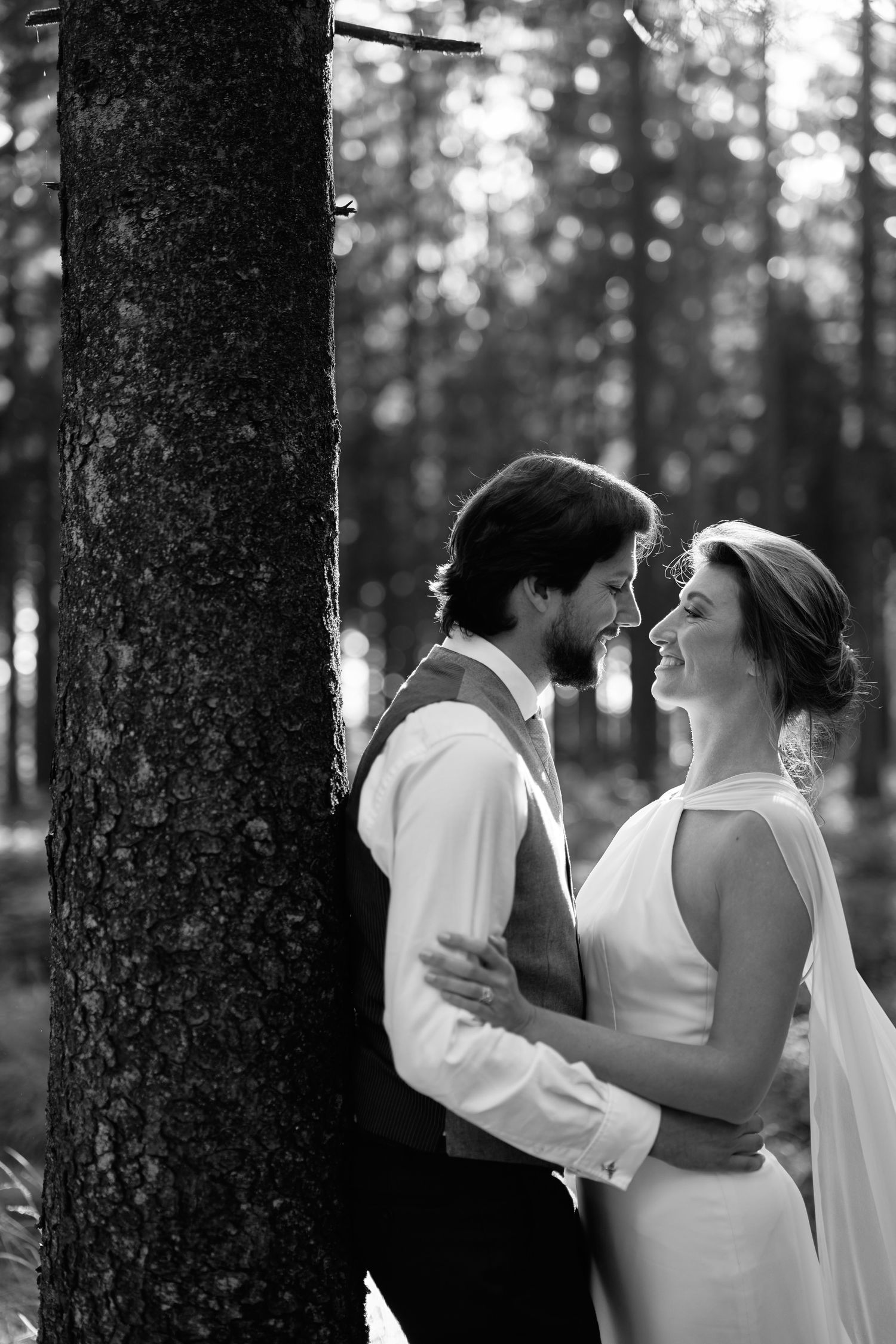 Black and white romantic wedding photo sequence showing a couple embracing behind a tree in a forest setting.