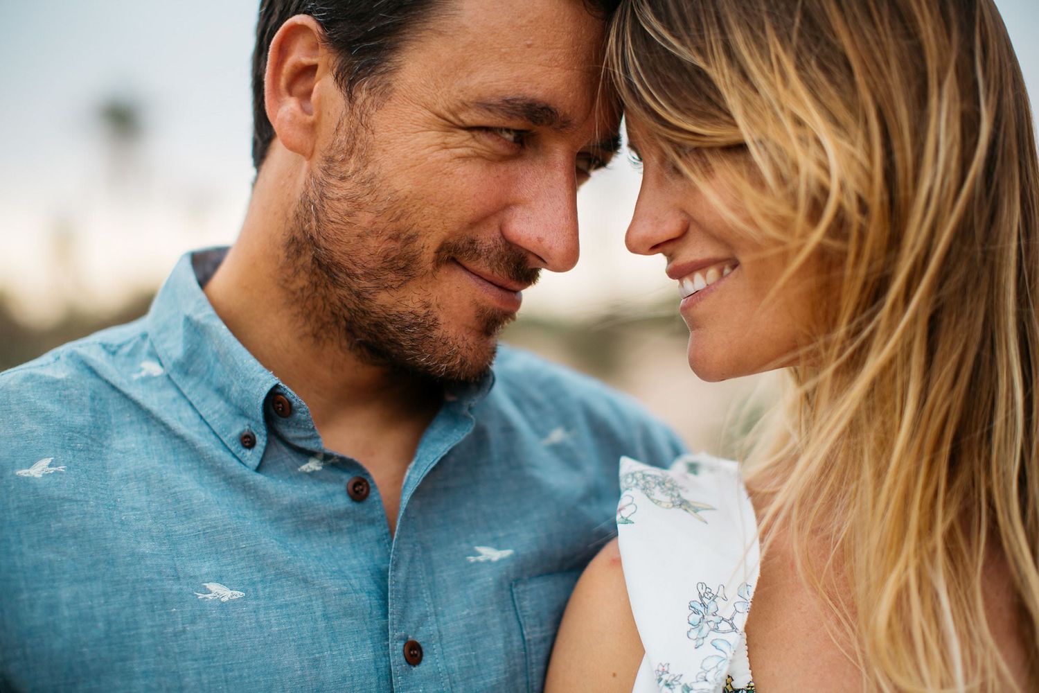 A romantic couple wearing matching blue shirts share an intimate moment outdoors.