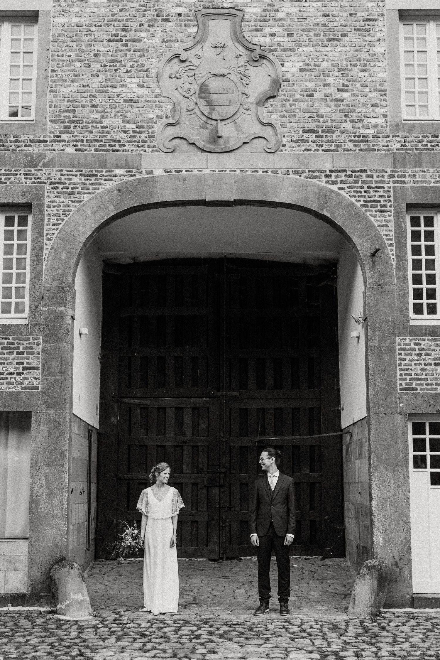 A series of four black and white photos showing a couple standing in front of a brick building with arched doorways.
