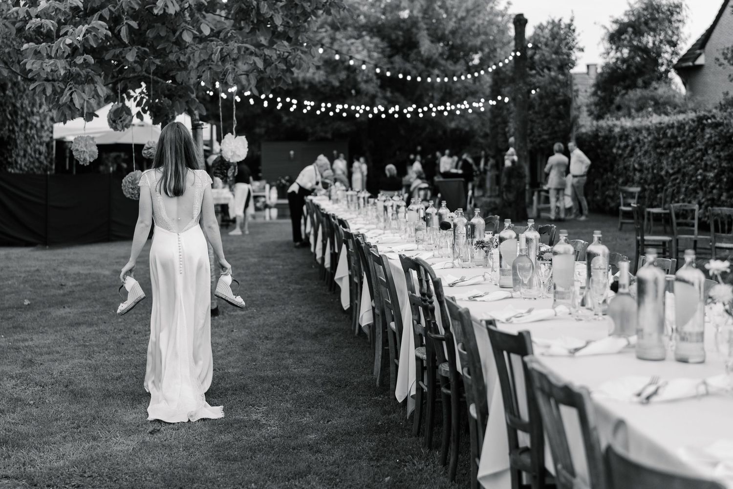 A series of black and white wedding photos showing an outdoor reception with long tables and string lights overhead.