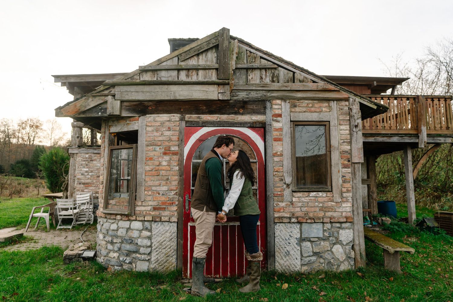 A panoramic view of an old stone building with red doors and windows set against a rural countryside landscape.