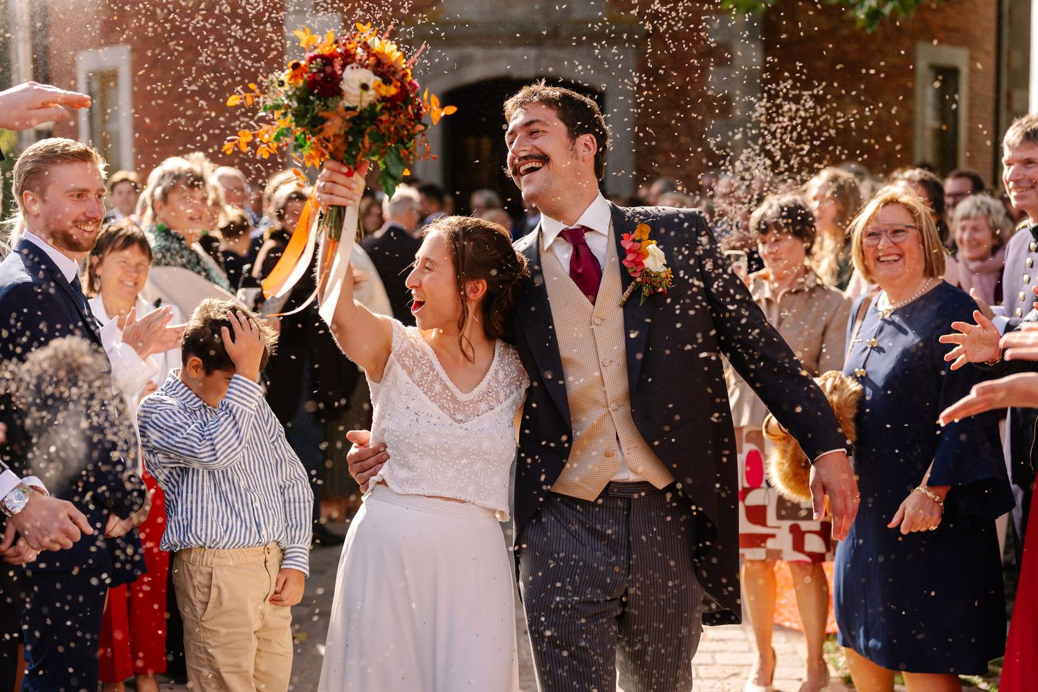 Wedding guests joyfully throw confetti and rice at a couple during an outdoor celebration ceremony.