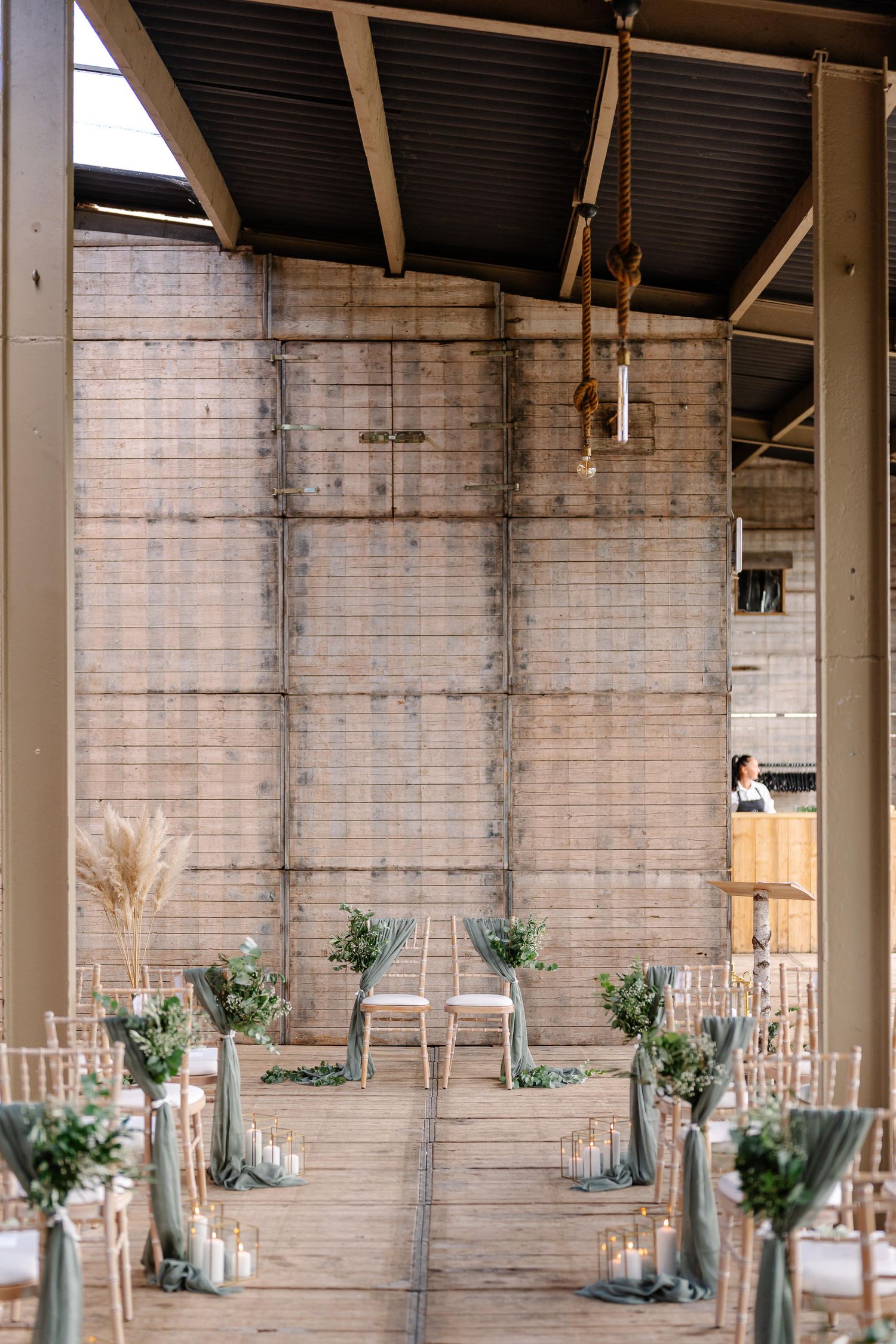Rustic industrial wedding reception venue with exposed brick walls and elegant table settings featuring glass vases and greenery.