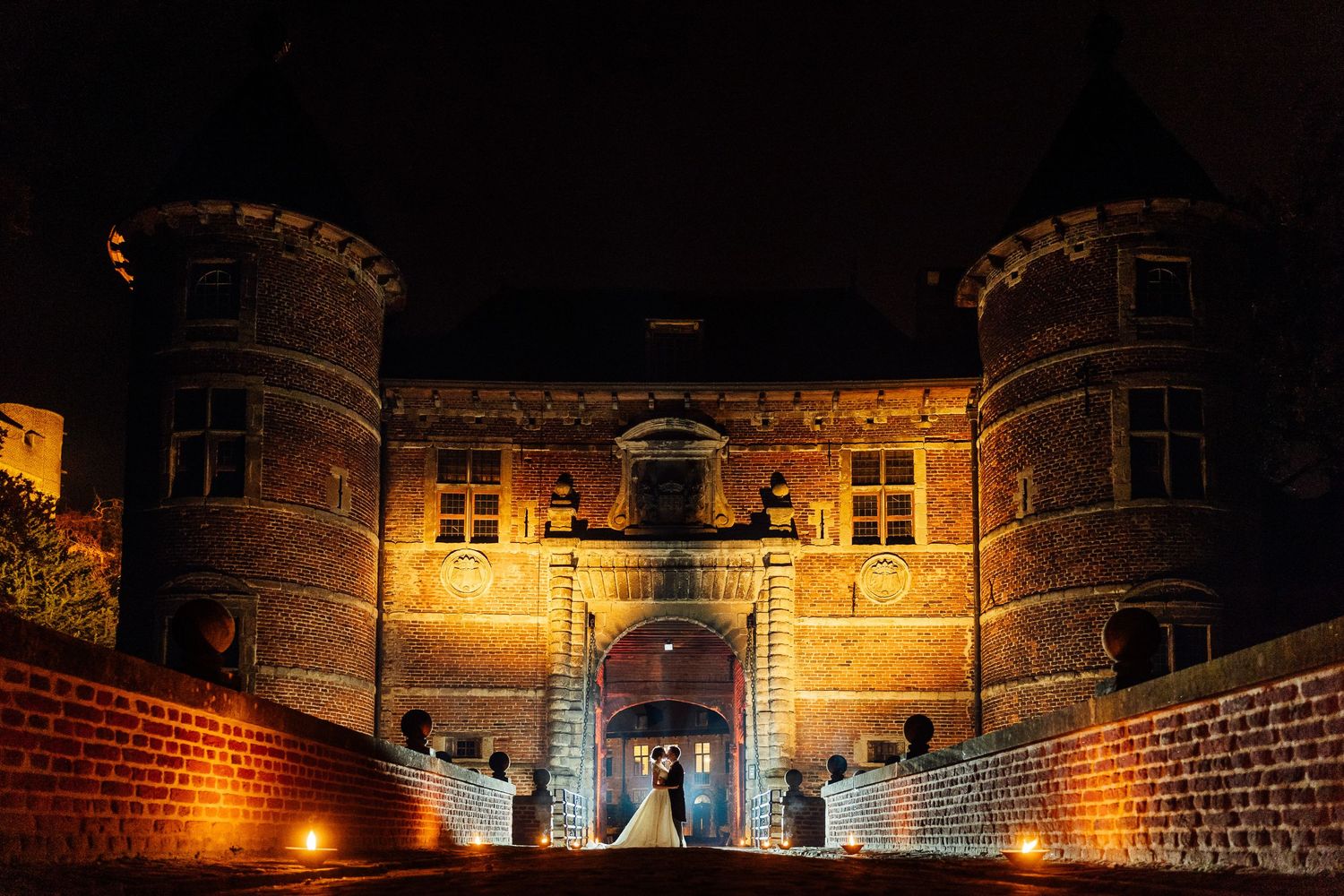 Stone castle walls illuminated by warm yellow lights at night create a dramatic medieval atmosphere.