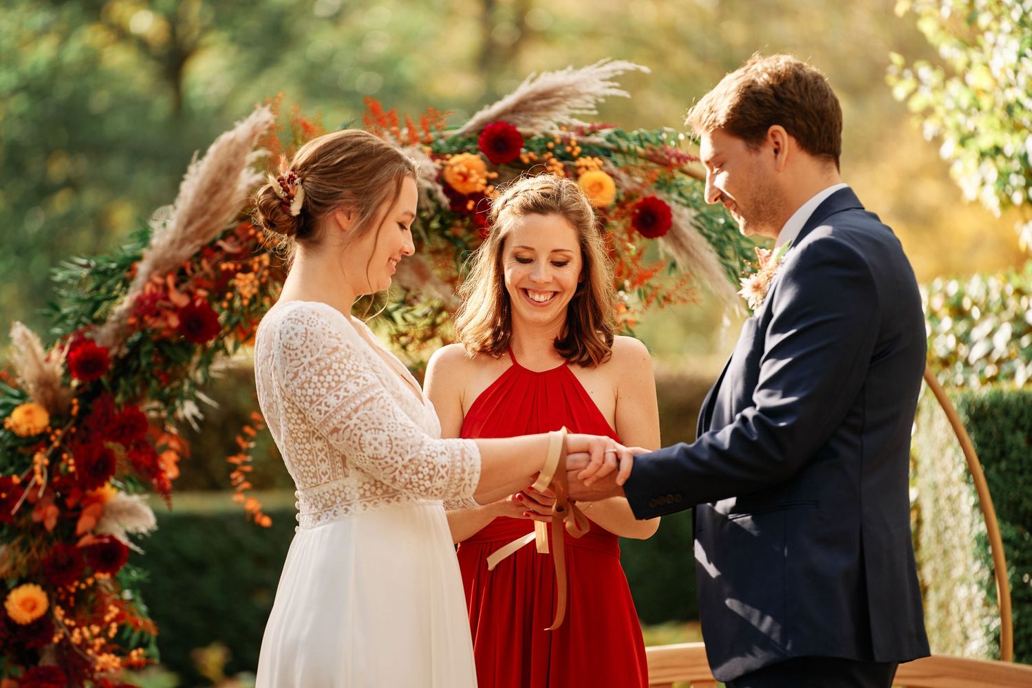A couple shares an intimate moment during their autumn wedding ceremony surrounded by vibrant red floral arrangements.