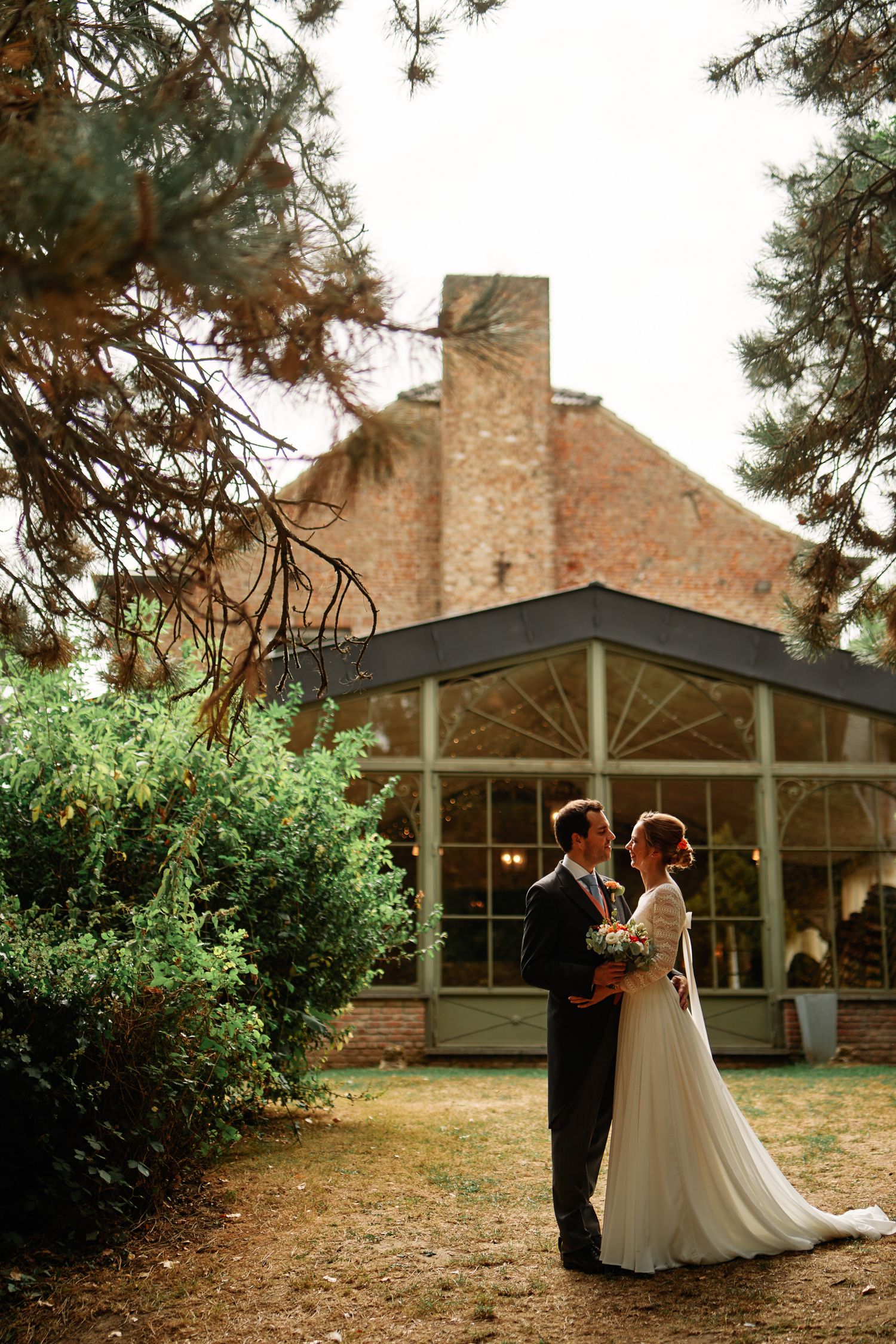 Elegant wedding ceremony venue with rustic brick building and pine trees creating a romantic outdoor setting.