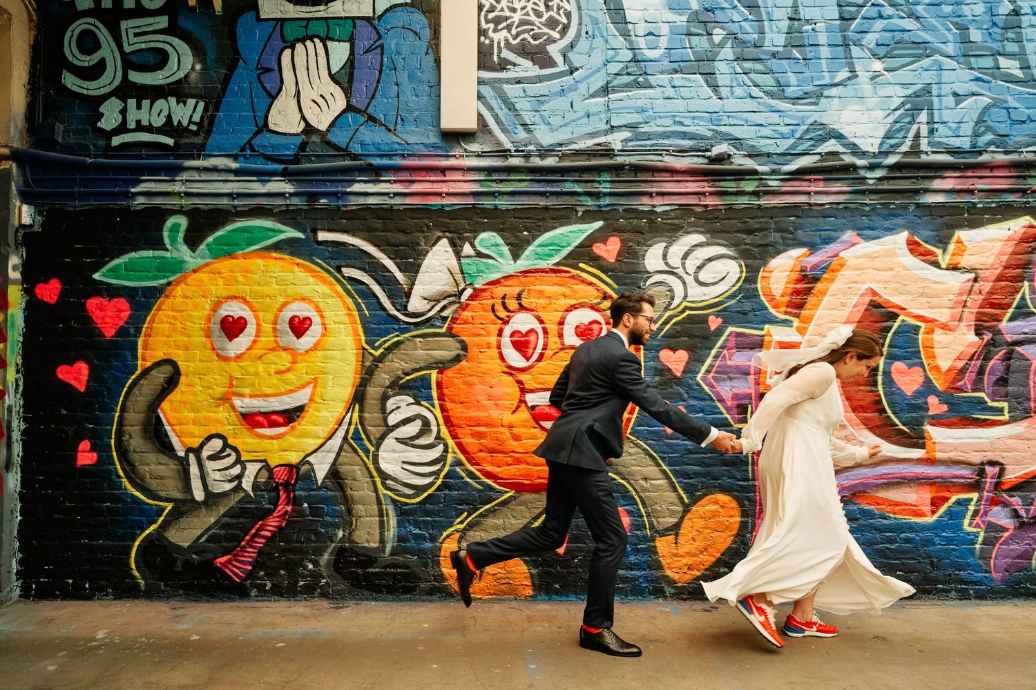 Colorful graffiti art murals featuring cartoon characters and abstract designs decorate a long outdoor wall.