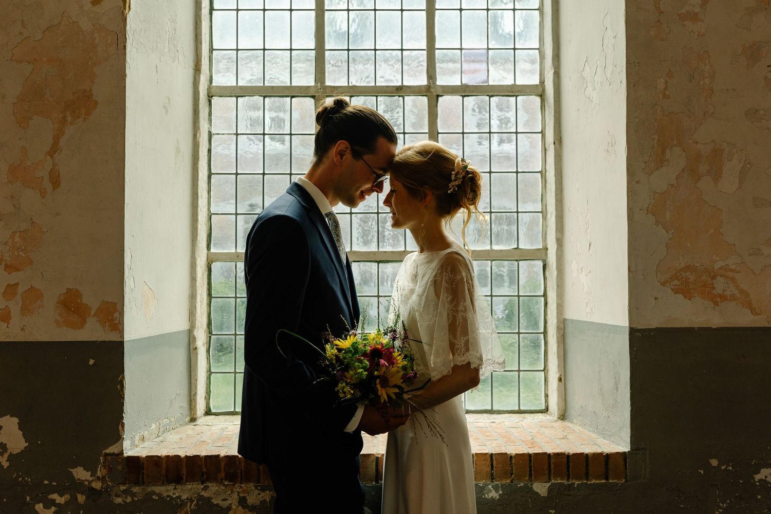 Couple in vintage room with large windows creating dramatic natural lighting.
