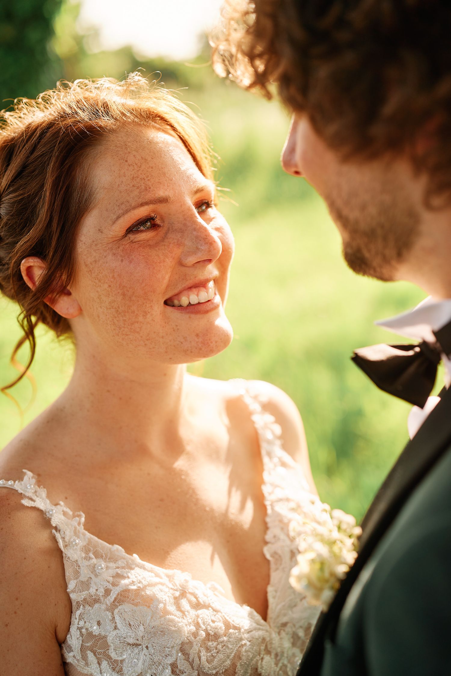 A romantic wedding moment captured in golden sunlight as a bride in lace gazes lovingly at her partner.