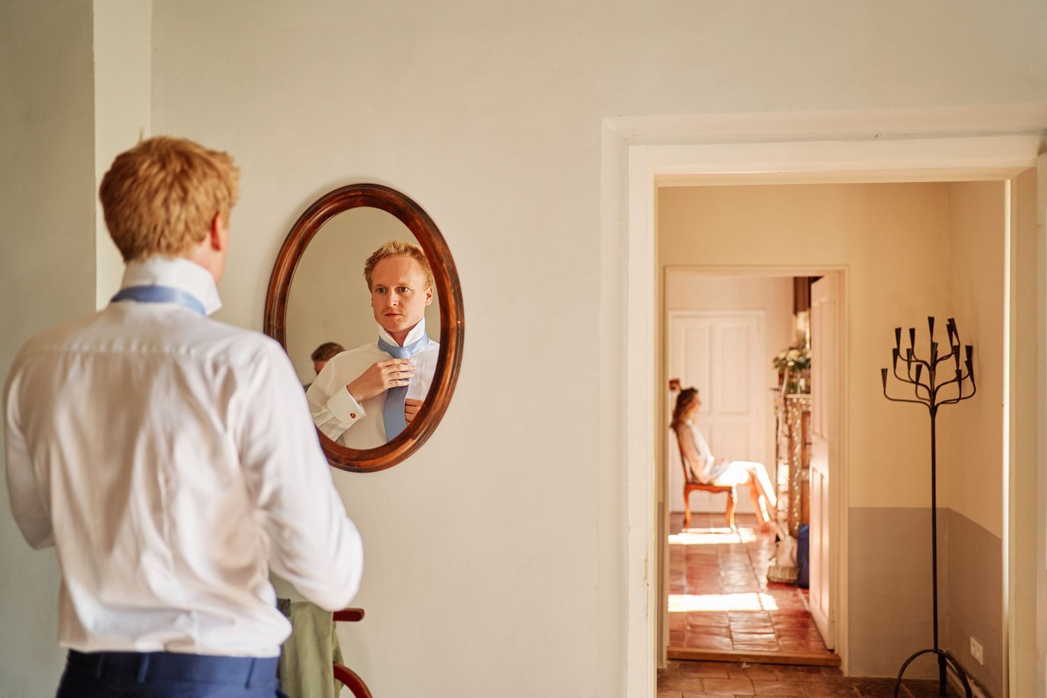 A white dress shirt reflection in a round mirror with a doorway and candelabra visible in the background.