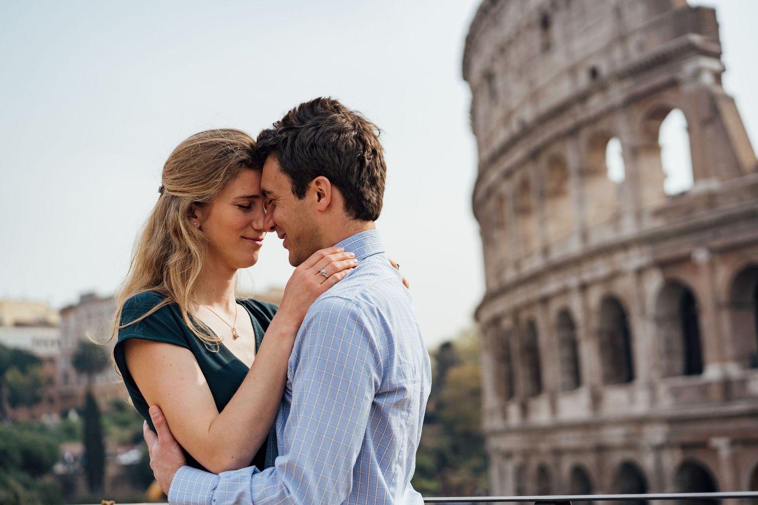 A couple shares romantic moments in front of the historic Colosseum in Rome during a sunny day.