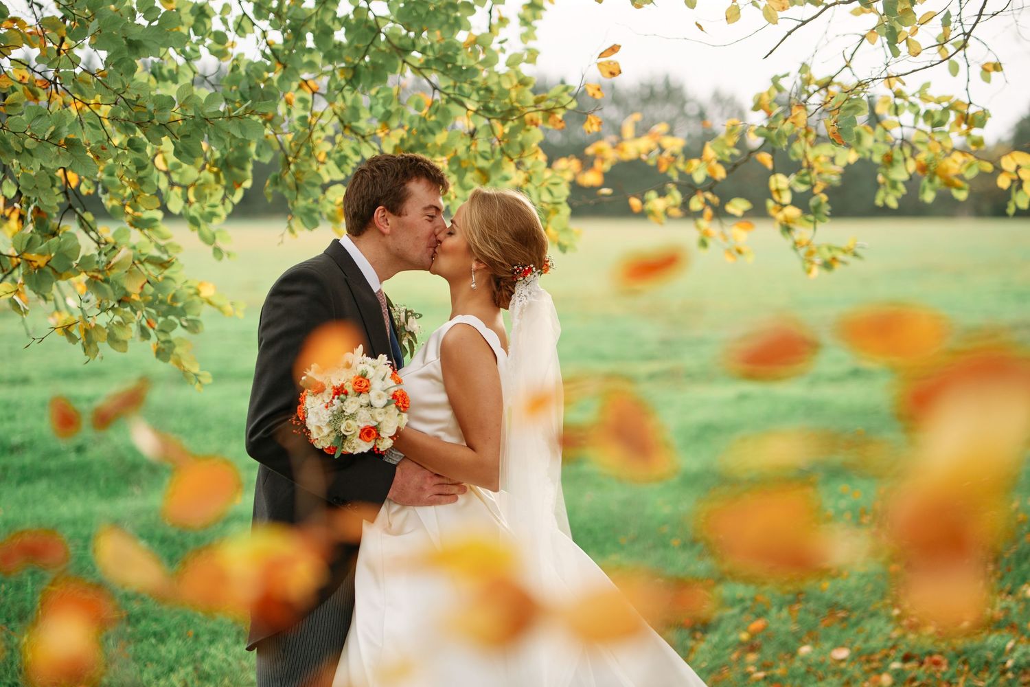 Romantic couple shares a tender kiss in a garden setting with orange flowers in the foreground creating a dreamy atmosphere.