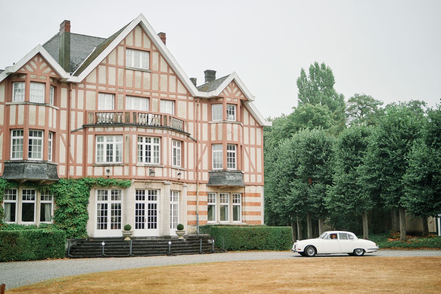 Historic Tudor-style mansion with ornate woodwork and multiple wings sits on a manicured estate property.