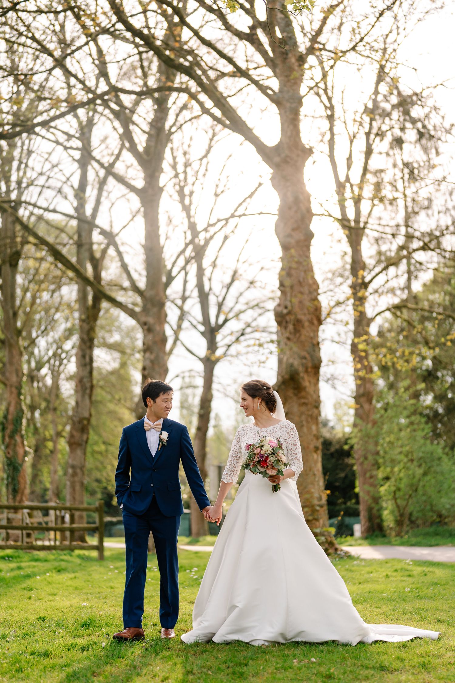 A romantic wedding couple shares tender moments in a sunlit spring garden with blooming trees and lush grass.