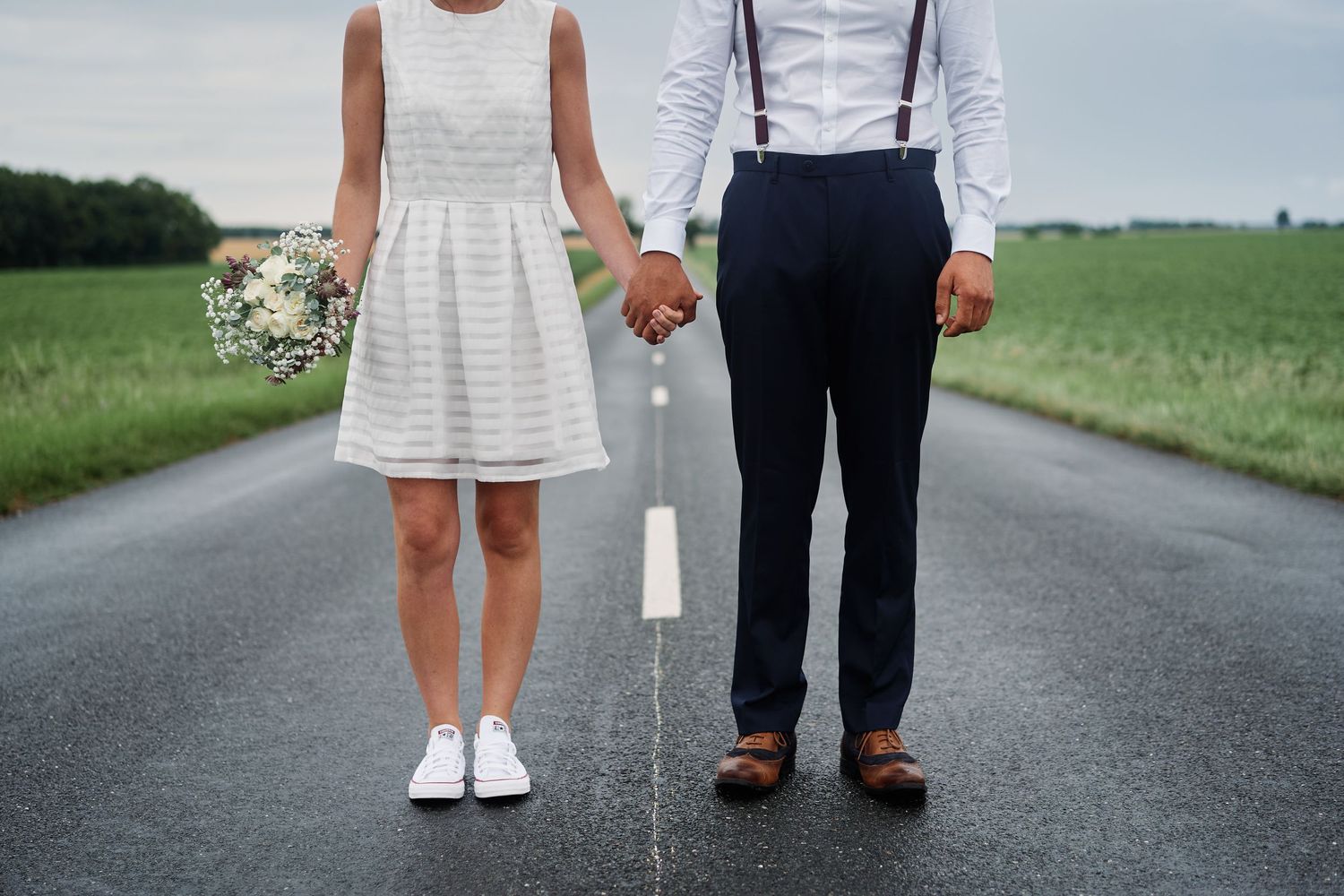 Cropped view of couple in wedding attire standing together on a paved road in a rural setting.