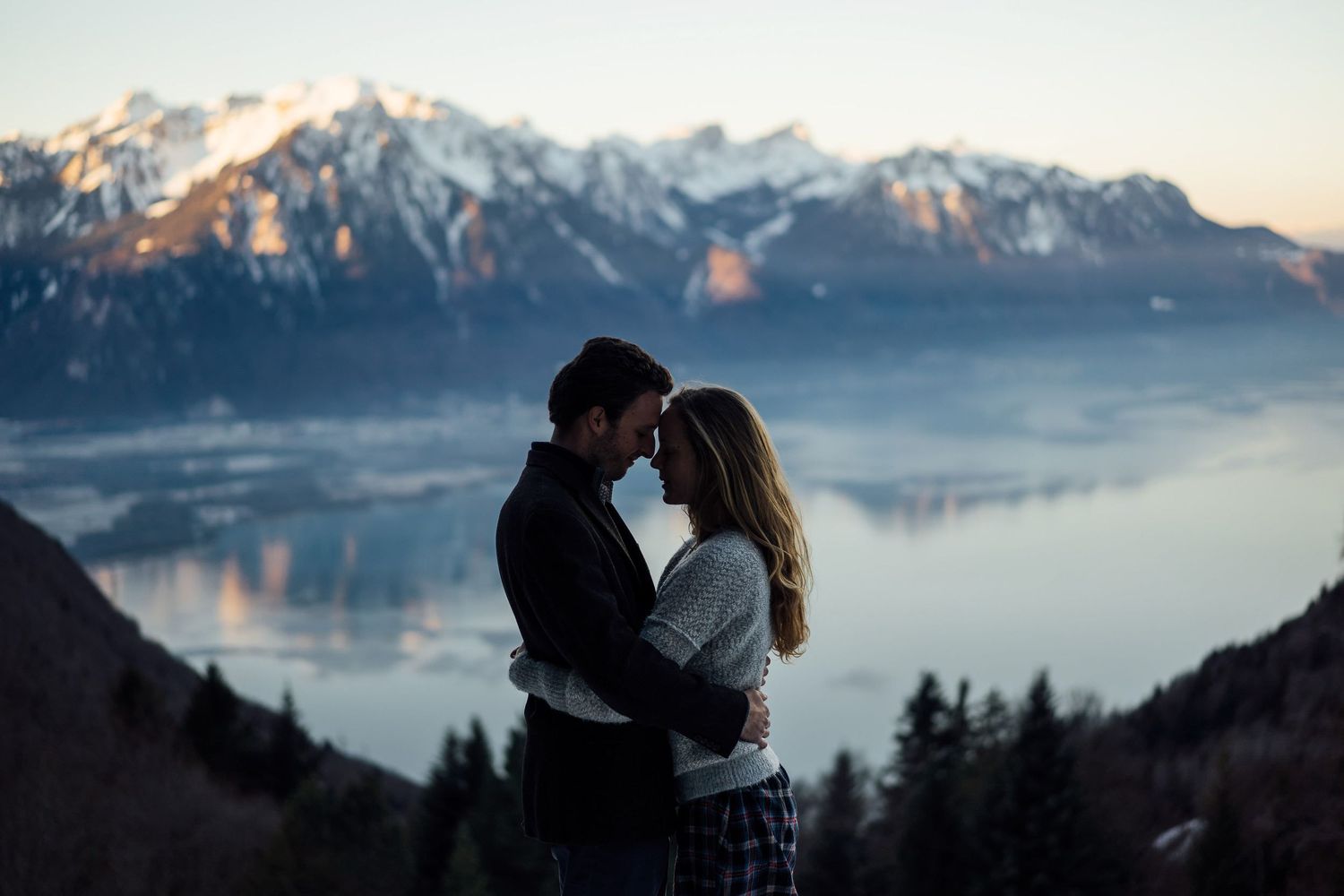 Silhouetted couple sharing an intimate moment against majestic mountain backdrop during sunset.