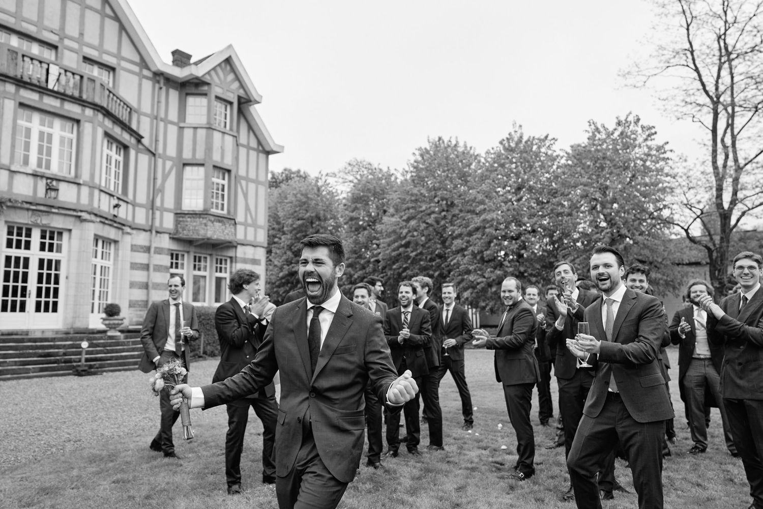 A group of formally dressed people walking and conversing outside a traditional brick building on a cloudy day.